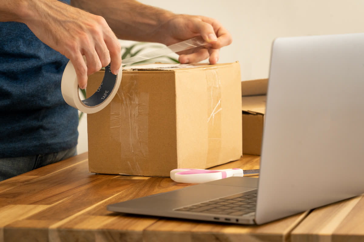 Sealing a parcel while booking shipping on a laptop — 스마트 스토어 창업 방법, 6단계 순서와 걸리는 기간